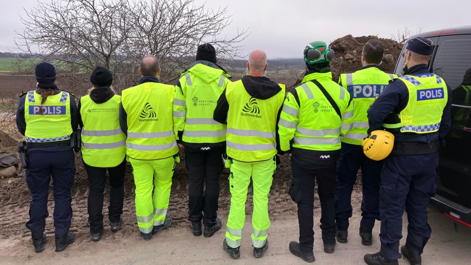 Åtta statstjänstepersoner med reflexvästar med respektive myndighets logotyper på står med ryggarna vända.