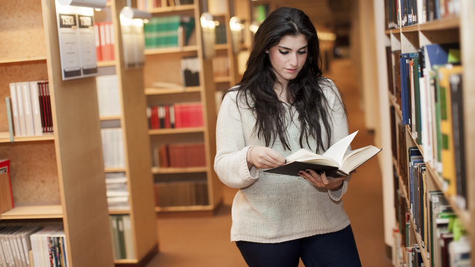 Kvinnlig student läser på högskolans bibliotek. 