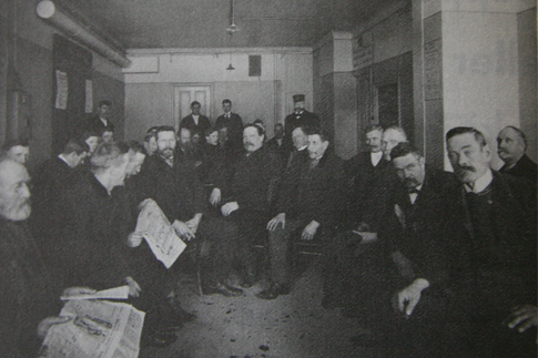 Svartvit bild på en samling män som sitter i ett trångt väntrum.