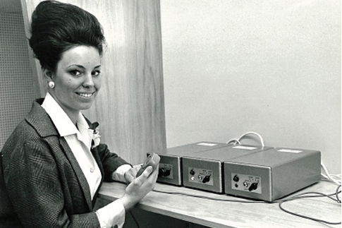 Young woman with a beehive hairdo next to a radio transmitter.
