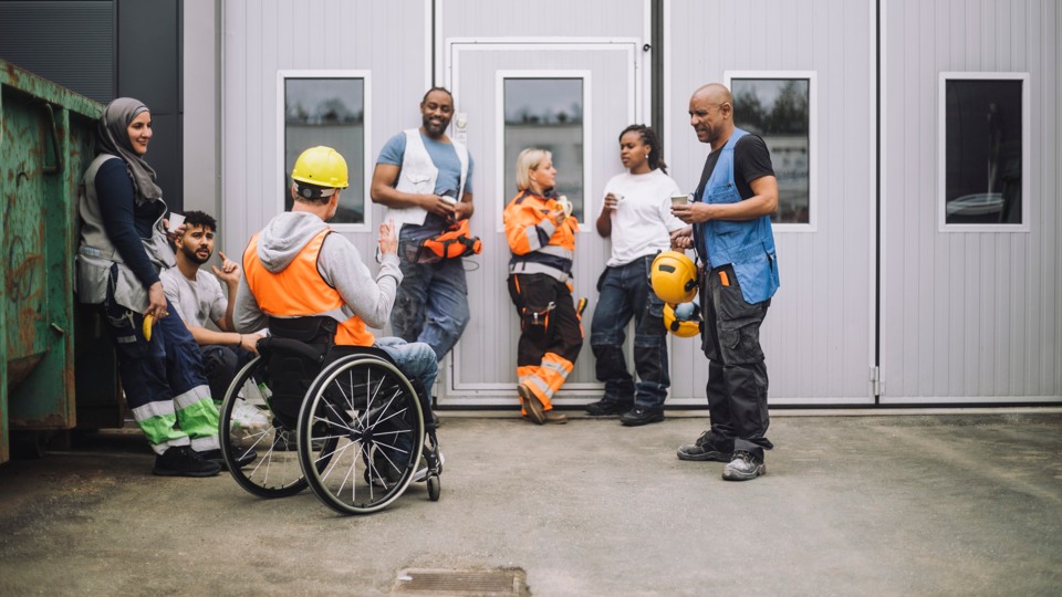 En grupp av människor i byggarbetskläder som står och pratar framför en garageport.