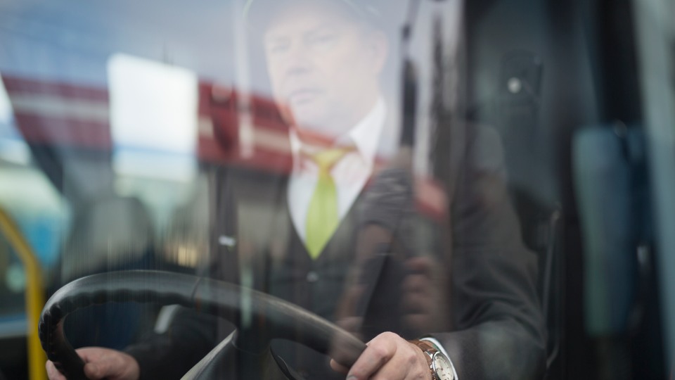 Manlig bussförare syns genom framrutan på bussen.