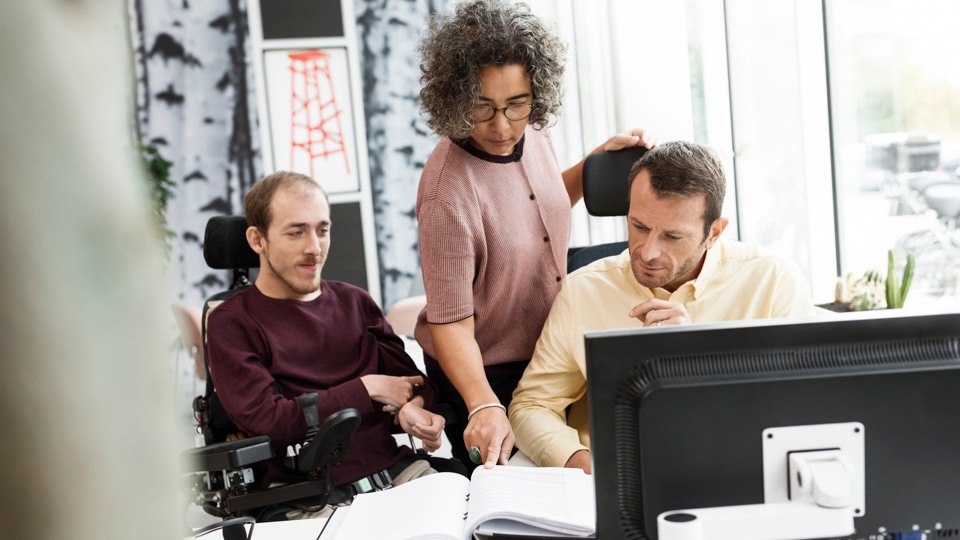 Tre män i samtal vid en laptop