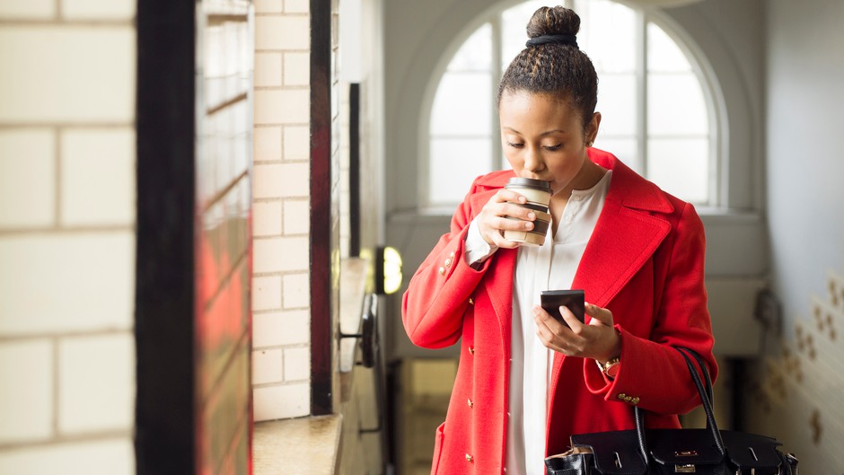 Kvinna som dricker kaffe och tittar på sin mobiltelefon